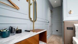 Une salle de bain moderne avec un comptoir en marbre, des meubles en bois, un miroir encadré d’or et un mur orné d’un motif.