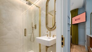 Une salle de bain moderne avec une douche à parois de verre, un lavabo blanc doté de robinetterie dorée et un grand miroir.