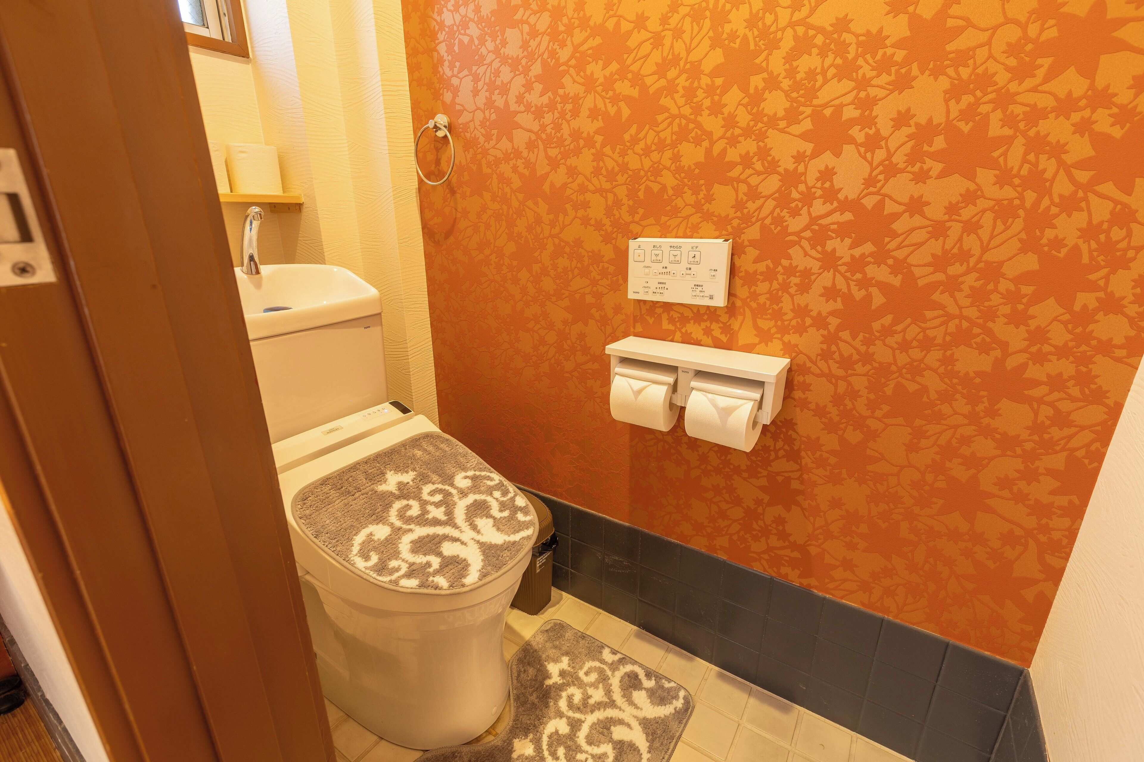 A bathroom with a toilet, sink, and towel dispenser.
