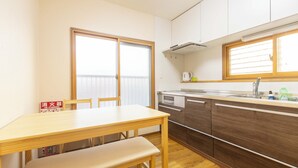 Une cuisine compacte avec une table et un banc en bois, un four encastré et une fenêtre équipée de stores.
