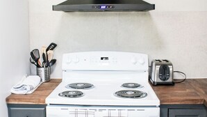 A kitchen with a white stove, a black range hood, and a toaster on the counter. - Golfers Oasis Centrally Located (Aiken)