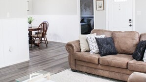 A living room with a brown sofa, a glass coffee table, and a dining area with a wooden table and chairs. - Golfers Oasis Centrally Located (Aiken)