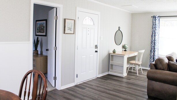 A room with a wooden dining table, a white desk with a chair, a brown sofa, and a door leading to another room. - Golfers Oasis Centrally Located (Aiken)