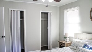 A bedroom with a bed, a nightstand, a bedside table, and two open closets. - Golfers Oasis Centrally Located (Aiken)