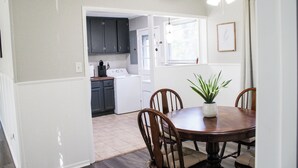 A dining area with a wooden table and chairs, a potted plant, and a view into the kitchen with dark cabinets and a white appliance. - Golfers Oasis Centrally Located (Aiken)