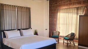 Un dormitorio con una cama grande, una pared de ladrillo, una ventana con cortinas y una silla.