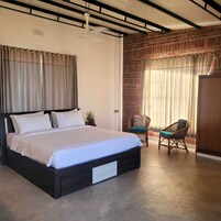 A bedroom with a large bed, a brick wall, a window with curtains, and a chair.