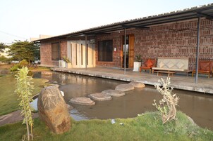 A brick house with a covered porch, a small pond with stepping stones, and outdoor seating.