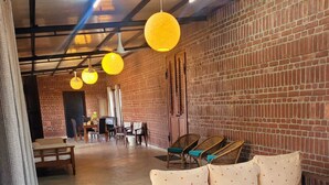 Un rincón de descanso acogedor con pared de ladrillo, un sofá con cojines de lunares, sillas de mimbre e iluminado por lámparas colgantes amarillas.