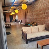 A cozy lounge area with a brick wall, a sofa with polka dot cushions, wicker chairs, and hanging yellow pendant lights.
