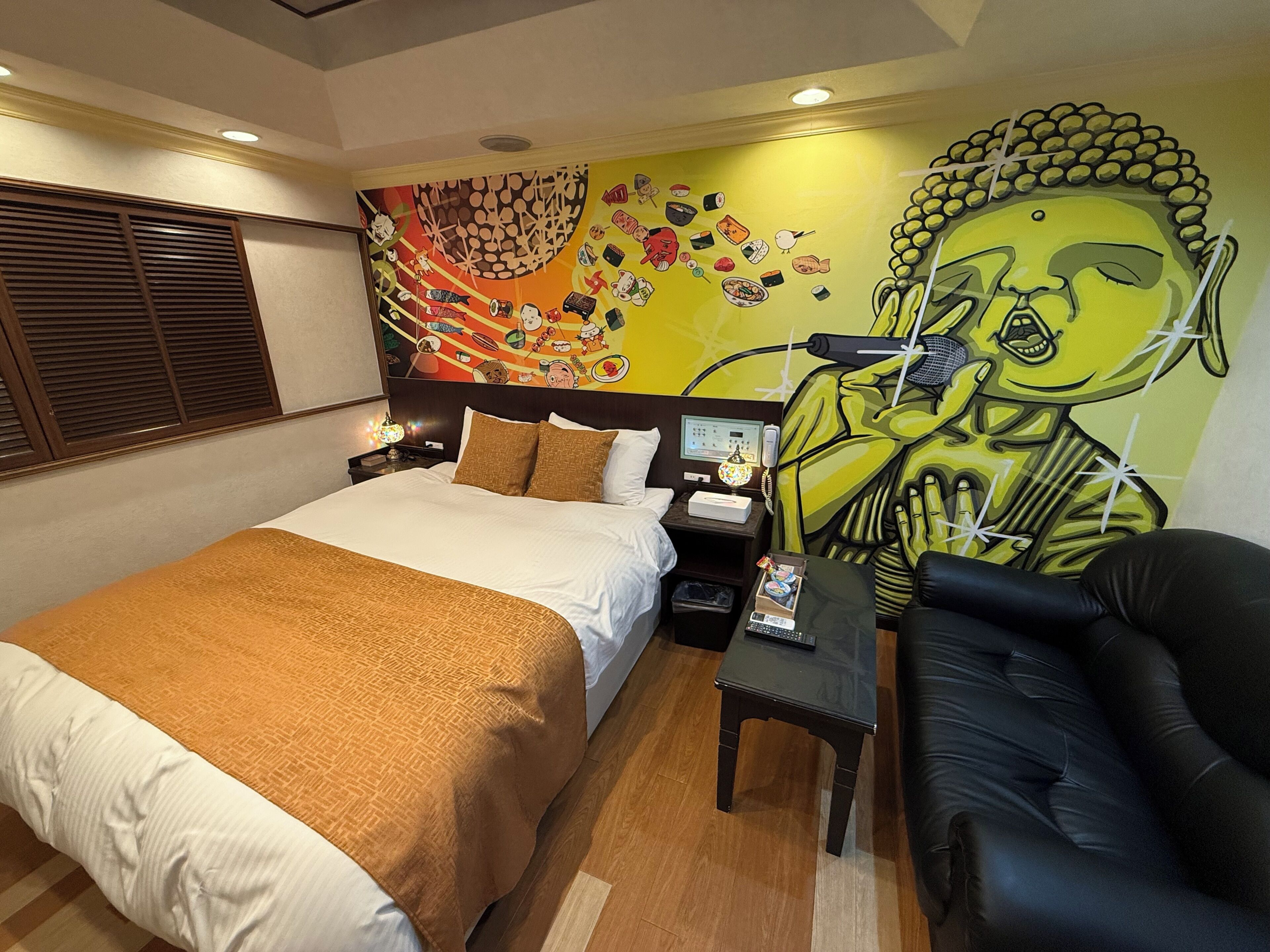 Habitación de hotel con cama, escritorio, silla, un mural en la pared y ventana con persianas.