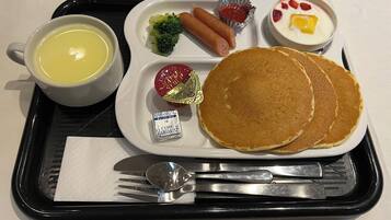 A tray with pancakes, hot dogs, broccoli, a cup of soup, and a small dish of fruit.