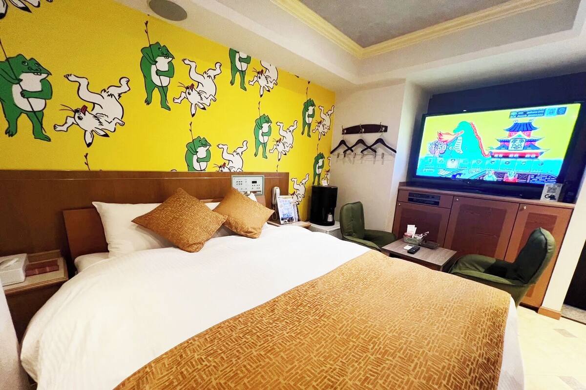 A hotel room with a large bed, a TV, and a wall mural.