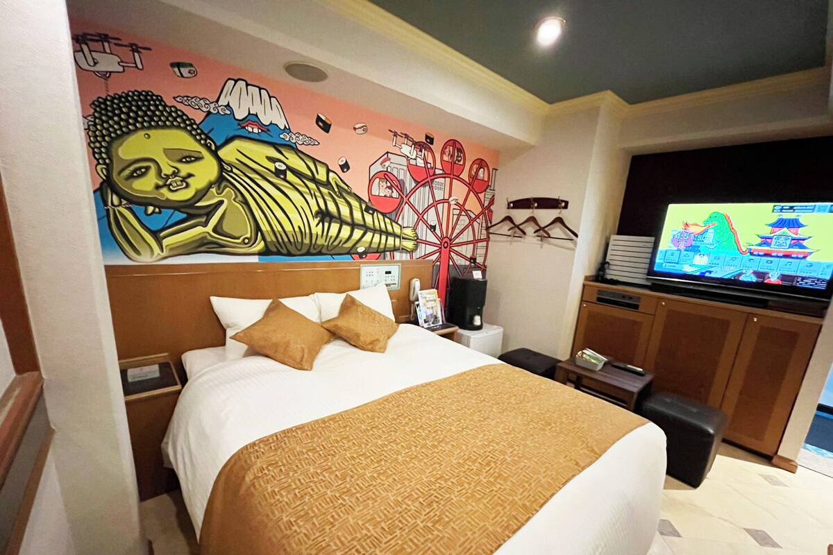 A hotel room with a large bed, a television, a mural on the wall, and a desk with a computer.
