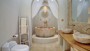 Ein Badezimmer mit einer Steinbadewanne, zwei Waschbecken, einem Holzschrank und einem Spiegel sowie einem Handtuchhalter.