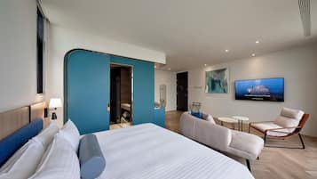 A modern hotel room with a large bed, a seating area with a sofa and chairs, a television, and a bathroom with a shower and a toilet.