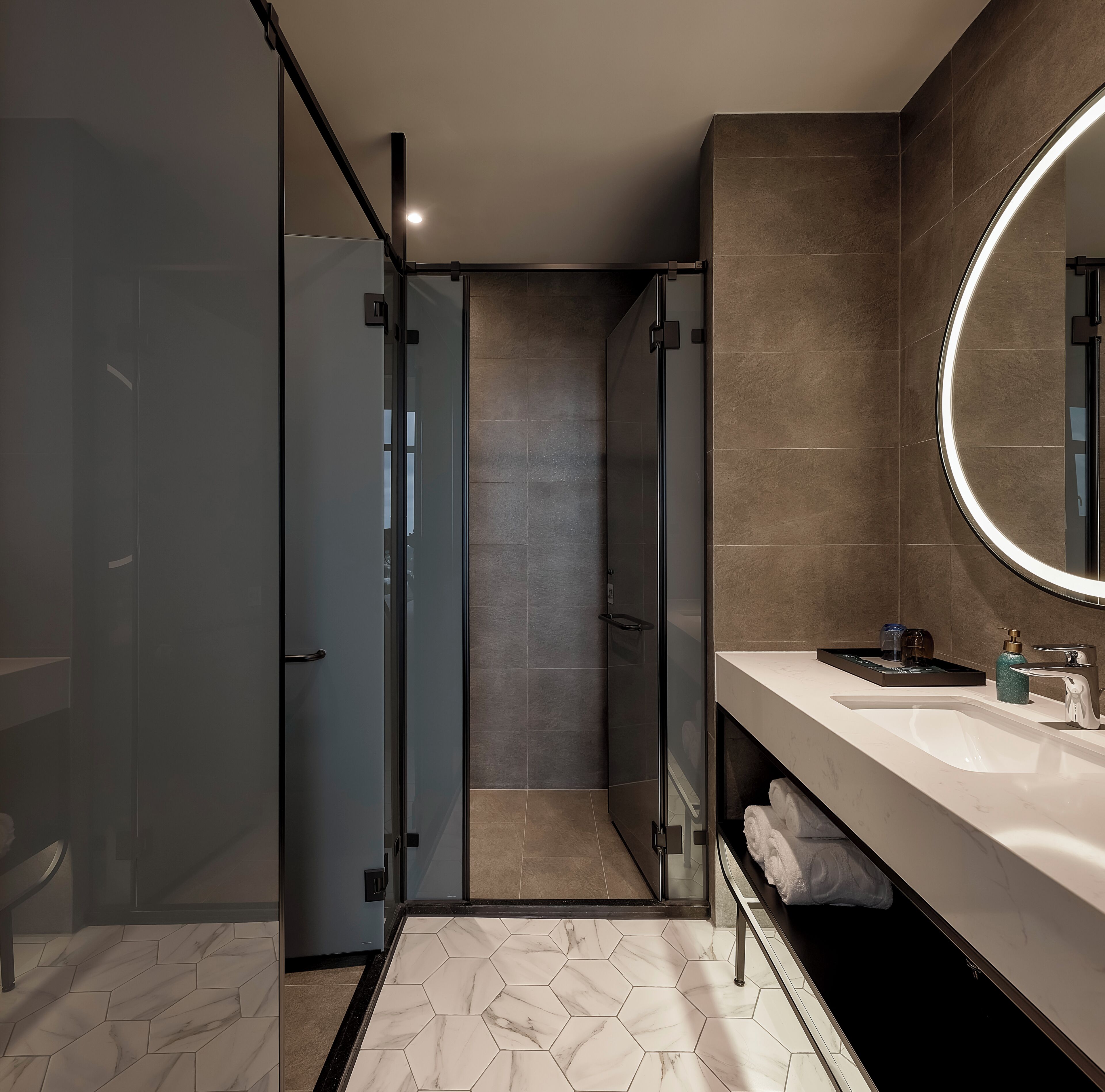 Un baño moderno con ducha envuelta en vidrio, tocador con espejo y suelo de mármol.