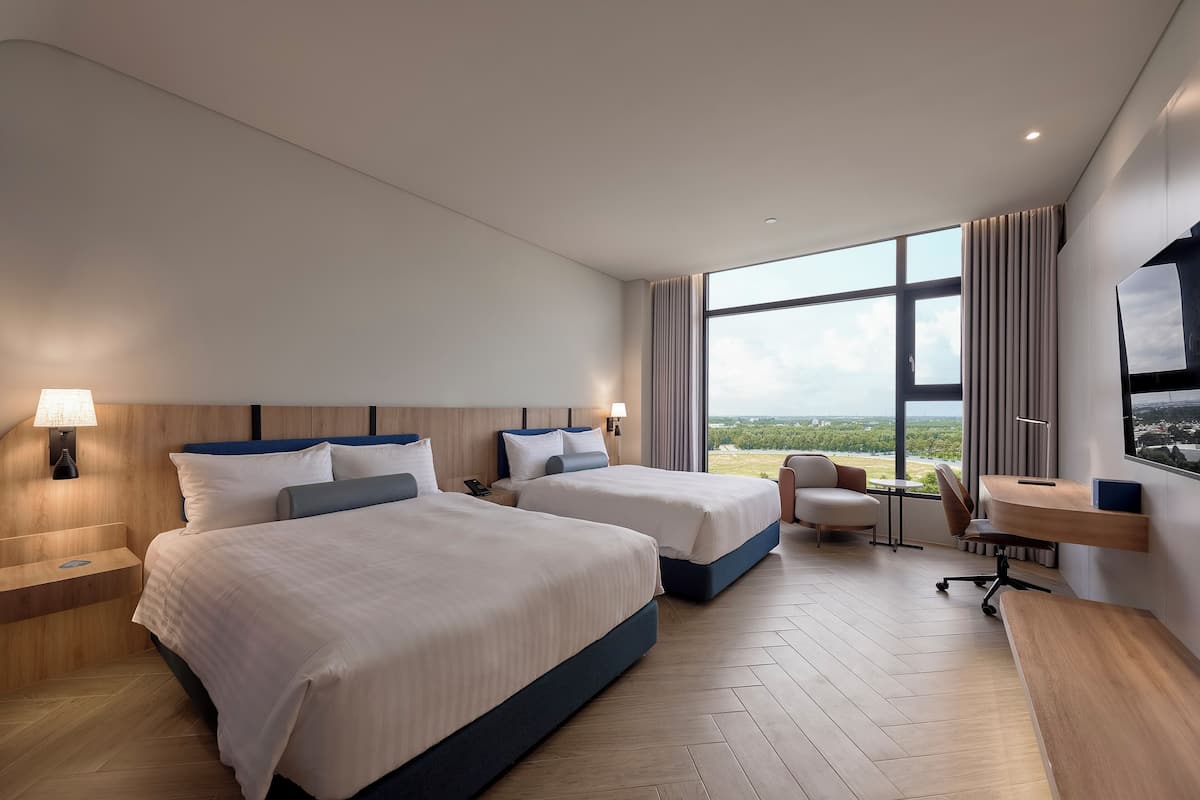 Une chambre d’hôtel moderne équipée de deux lits, d’un bureau, d’une chaise et d’une grande fenêtre donnant sur un paysage agréable.