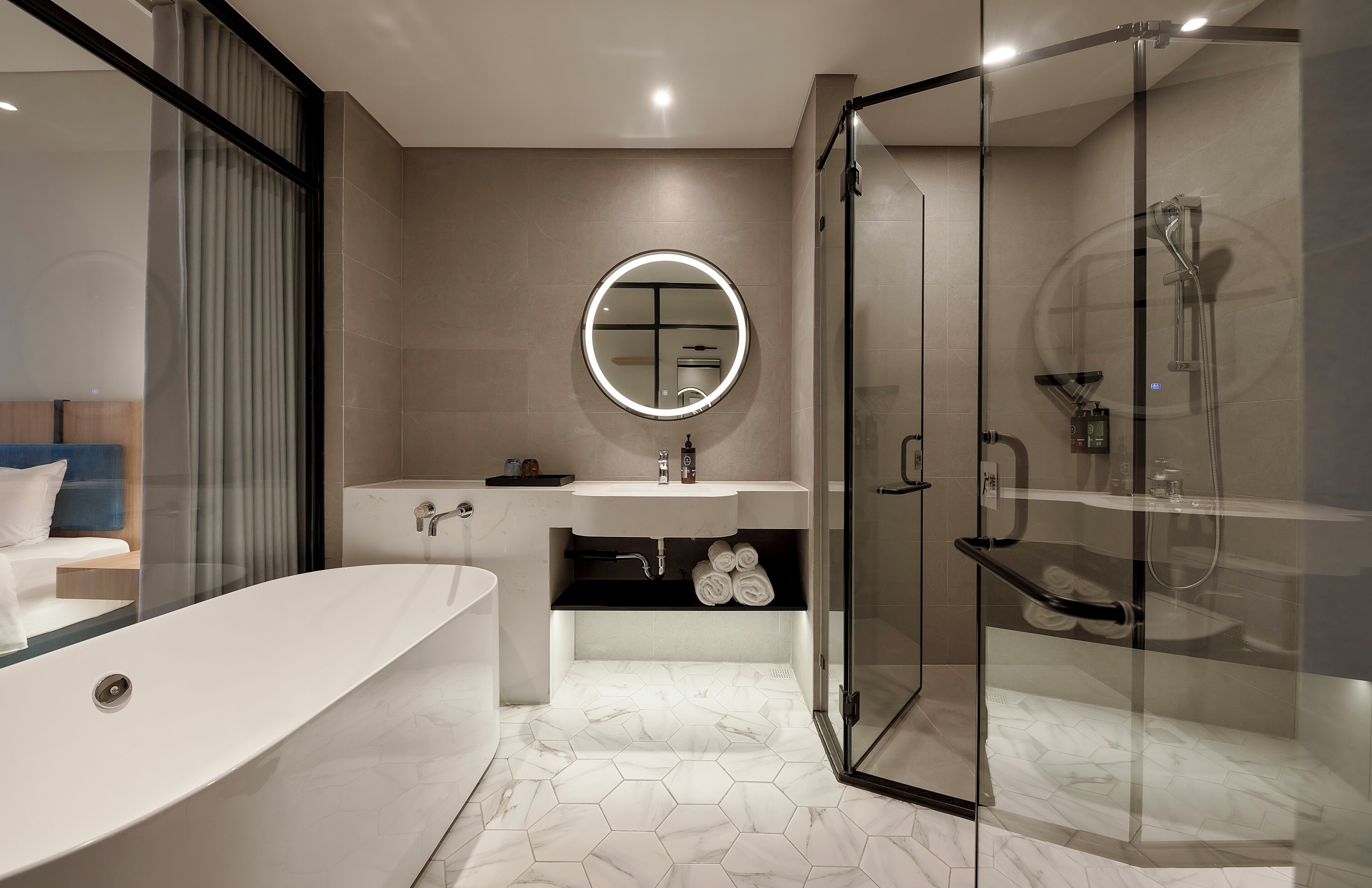 Un baño moderno con una bañera independiente, ducha con cerramiento de vidrio y un espejo redondo con luz.
