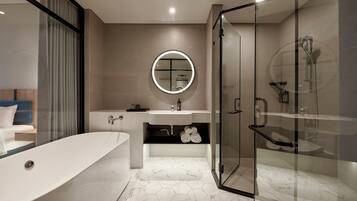 Un baño moderno con una bañera independiente, ducha con cerramiento de vidrio y un espejo redondo con luz.