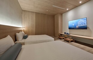 A hotel room with two beds, a desk, a TV, and a wooden ceiling.