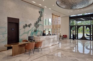 A modern reception area with a marble wall, a reception desk, and a large window offering a view of the outdoors.