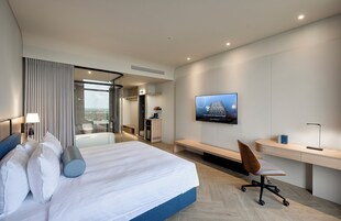 Una camera d'albergo moderna con un letto grande, una scrivania, una sedia, una televisione e vista sulla città.