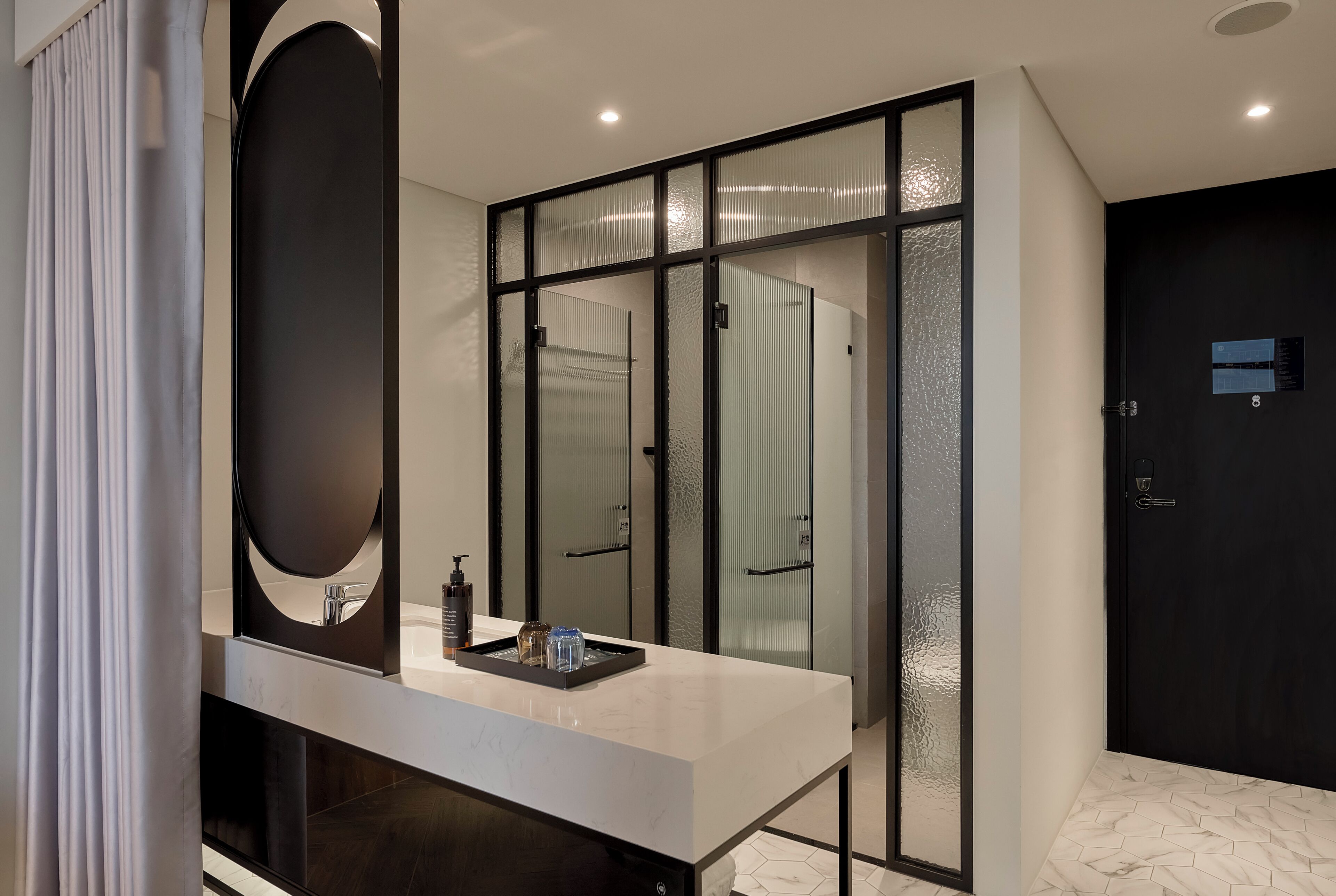Un baño moderno con un espejo grande, encimera blanca y puertas de vidrio esmerilado.