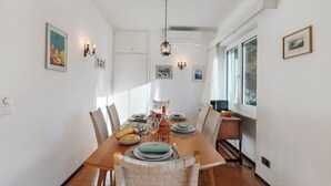 A dining room with a wooden table set for four, surrounded by chairs. There are wall-mounted lights and a hanging light fixture above the table.