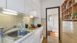 A kitchen with white cabinets, a stainless steel sink, and a wooden shelf with jars.