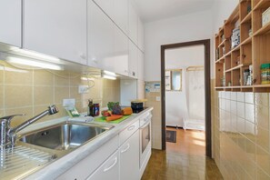 A kitchen with white cabinets, a stainless steel sink, and a wooden shelf with jars.