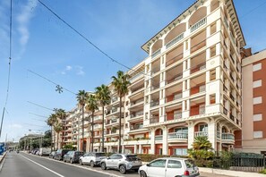 Un edificio de varios pisos con balcones, coches estacionados y palmeras.