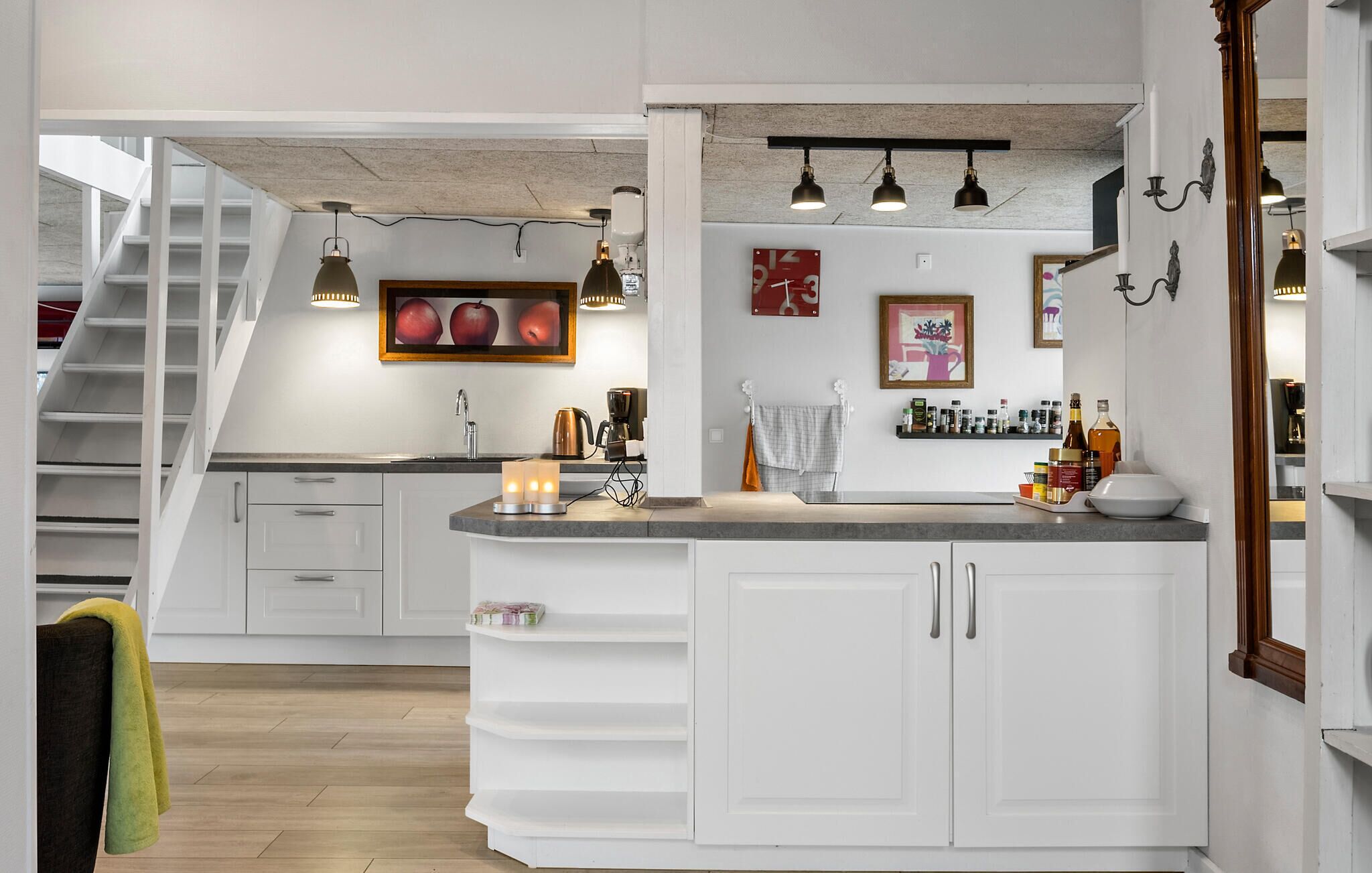 A modern kitchen with a central island, white cabinetry, and a staircase leading to an upper level.