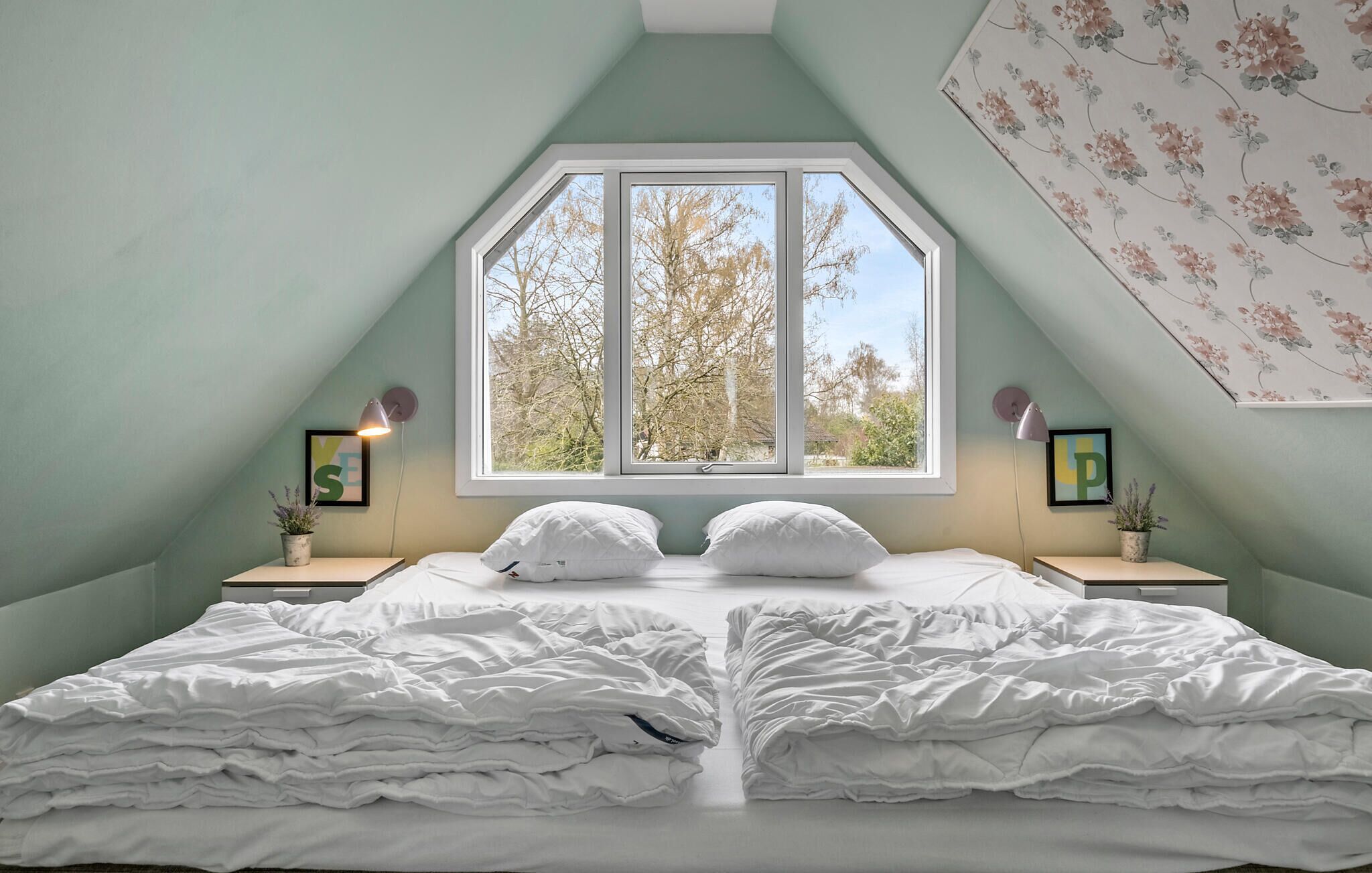 A bedroom with a large window, two bedside tables, and a bed with white bedding.