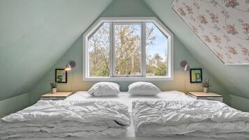 A bedroom with a large window, two bedside tables, and a bed with white bedding.