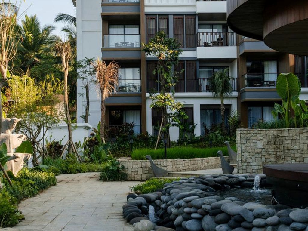 A modern building with multiple balconies, a stone pathway, and a water feature.