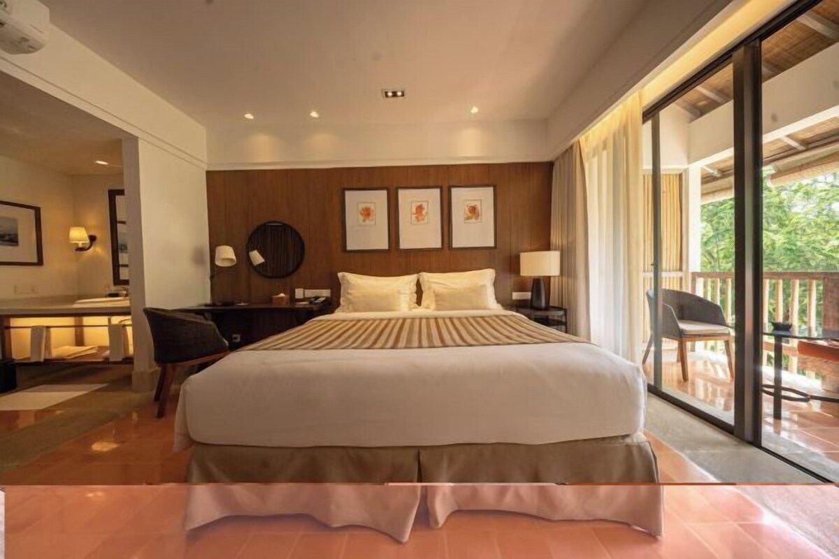A hotel room with a large bed, a desk, a chair, and a balcony with a view.