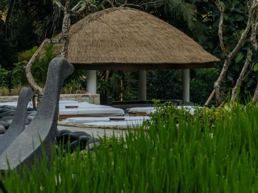 A thatched-roof structure with a stone base, surrounded by a garden with rocks and grass.