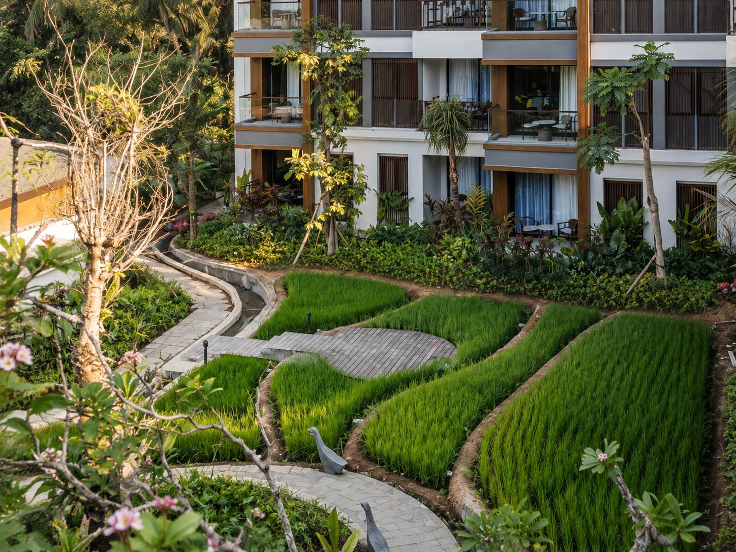 A modern hotel with multiple balconies, a landscaped garden with terraced greenery, and a clear view of the surrounding natural environment.
