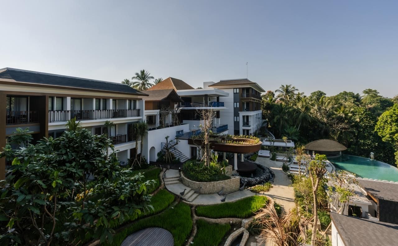A multi-story hotel with a pool, lush greenery, and a central water feature.