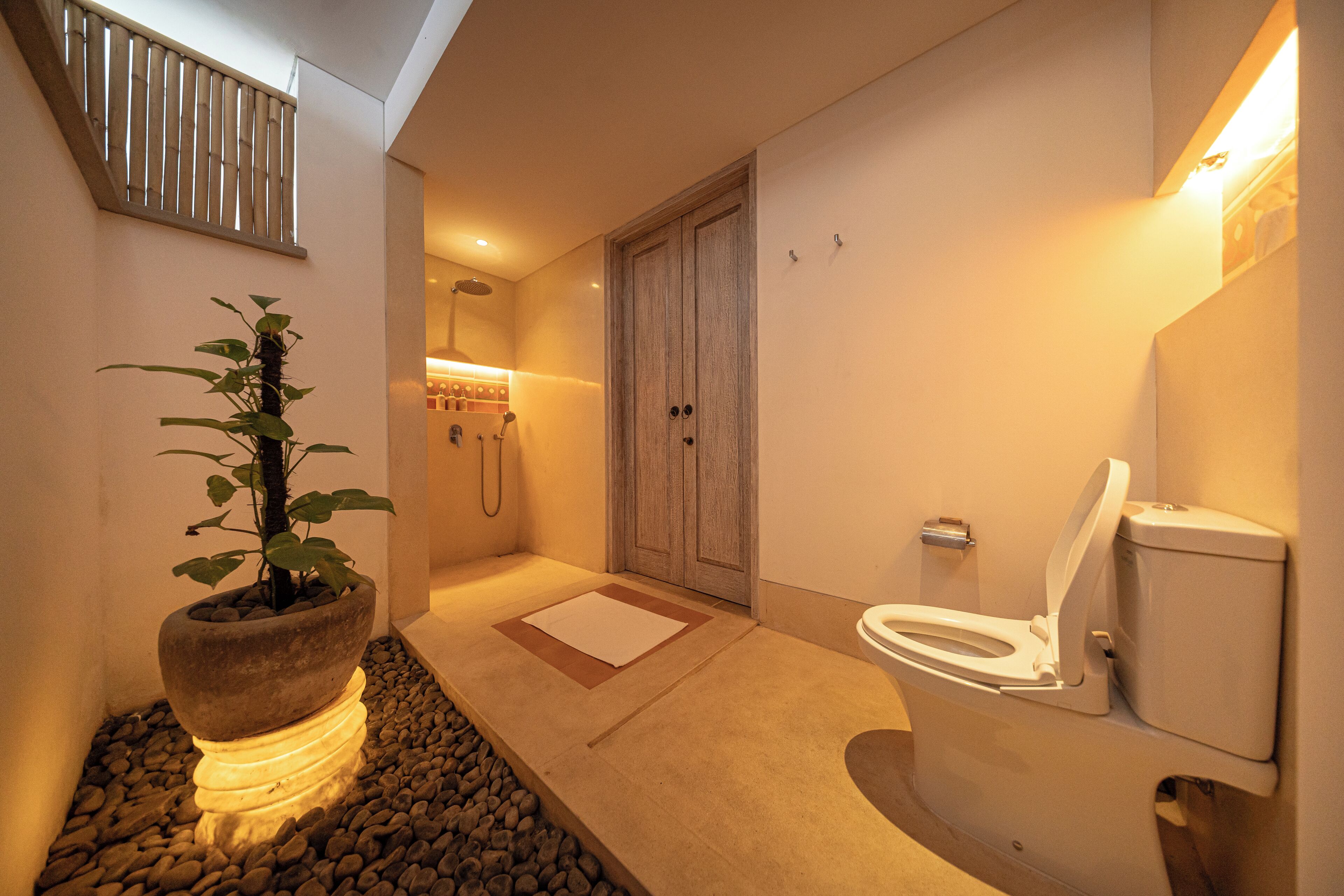 A modern bathroom with a shower, toilet, and a potted plant.