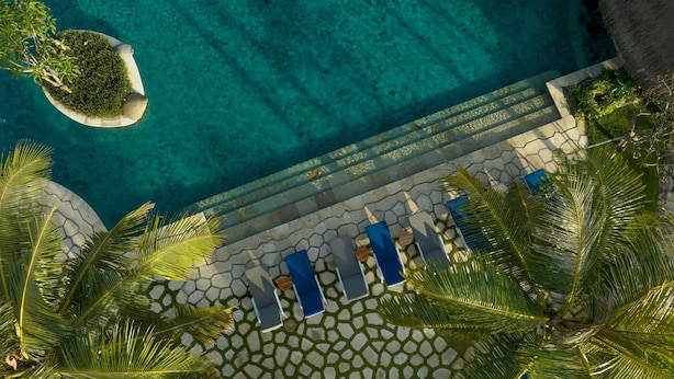 An aerial view of a pool area with clear blue water, surrounded by palm trees and lounge chairs. - Sudamala Resort Ubud Bali (Ubud)