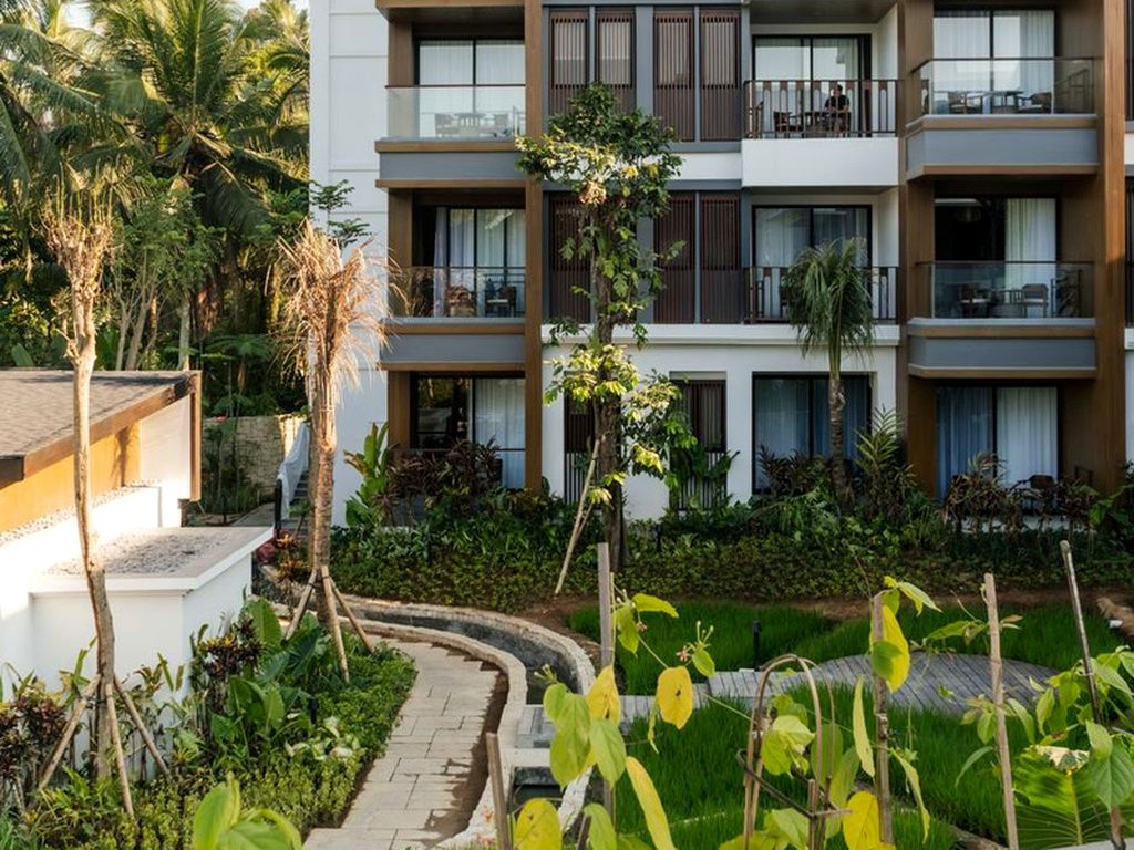Ein mehrstöckiges Hotel mit Balkonen, einem angelegten Garten und einem Weg.