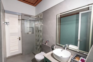 Un baño moderno con inodoro, ducha con puerta de vidrio, lavamanos con un espejo grande y tocador con un cesto de artículos de tocador.