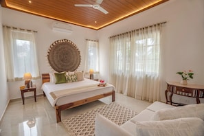 Un dormitorio con techo de madera, un gran tapiz circular en la pared, una cama con muchos almohadones, mesitas de noche con lámparas y una pequeña mesa de madera con un florero.