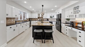 Une cuisine moderne avec des meubles blancs, un îlot central doté de tabourets de bar, une hotte de cuisine en acier inoxydable et un four encastré.