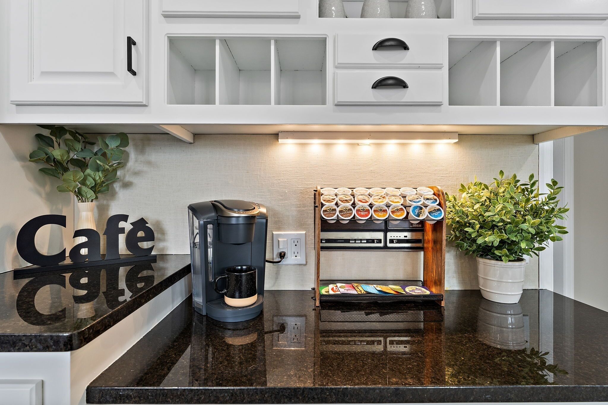 Una cocina con armarios blancos, una cafetera, un estante para especias y una planta en maceta.