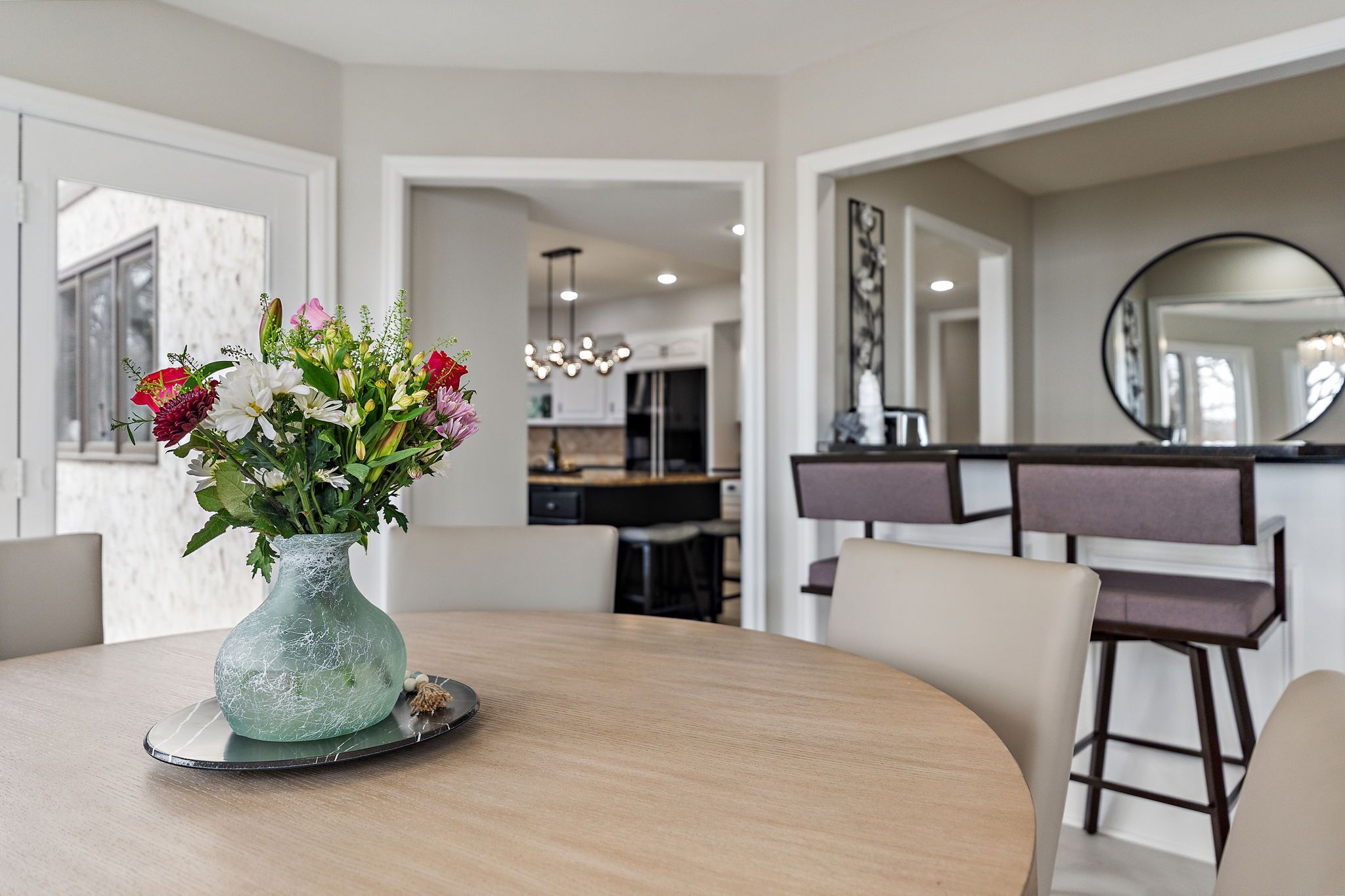 Un coin repas avec une table ronde, un vase de fleurs et, au fond, une cuisine moderne.