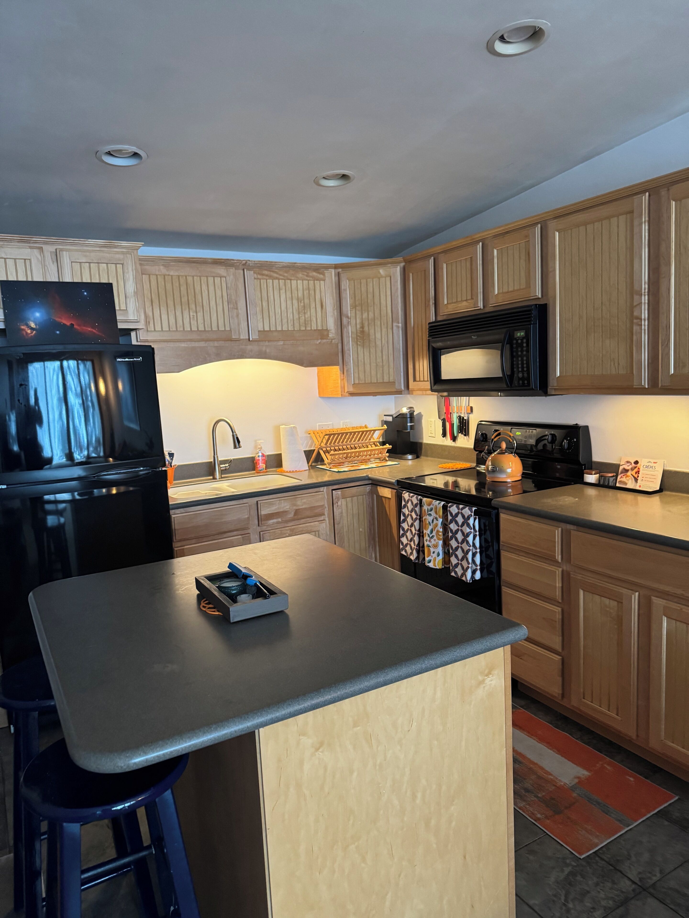 A modern kitchen with wooden cabinets, a black refrigerator, a microwave, and a coffee maker.