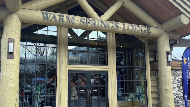 Exterior del Warm Springs Lodge, con fachada de madera, ventanas amplias y una pared de piedra.